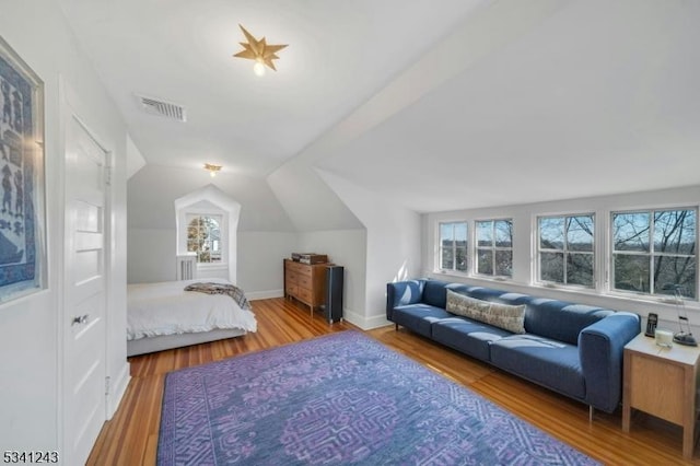 bedroom with vaulted ceiling, wood finished floors, visible vents, and baseboards