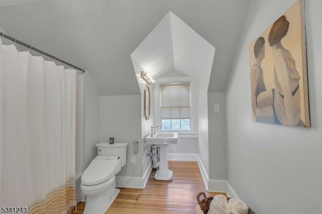 bathroom with baseboards, toilet, vaulted ceiling, wood finished floors, and a sink