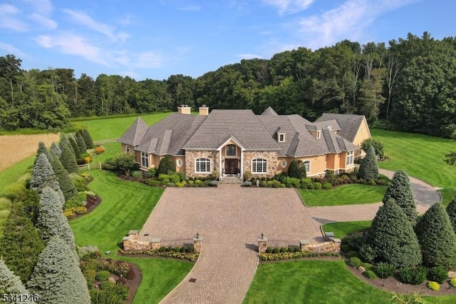 view of front of home featuring stone siding, a view of trees, decorative driveway, and a front yard