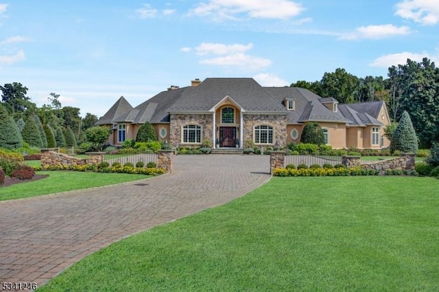 french country home featuring stone siding, fence, a front lawn, and decorative driveway