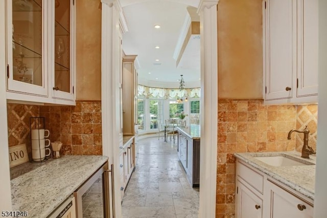 kitchen featuring wine cooler, stone tile flooring, glass insert cabinets, a sink, and light stone countertops