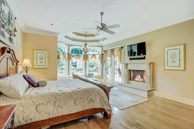 bedroom featuring crown molding, a raised ceiling, a high end fireplace, wood finished floors, and baseboards