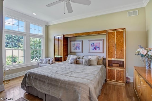 bedroom with ceiling fan, wood finished floors, visible vents, baseboards, and ornamental molding