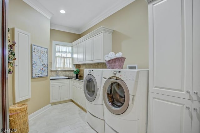 washroom featuring cabinet space, ornamental molding, washing machine and dryer, a sink, and baseboards