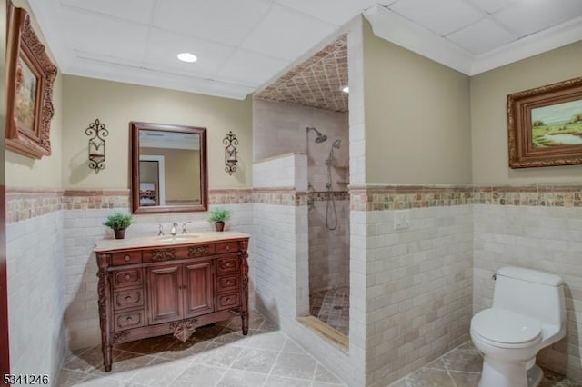 bathroom featuring tile patterned flooring, vanity, tile walls, tiled shower, and wainscoting