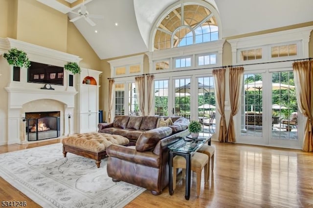 living area with high vaulted ceiling, a fireplace, ceiling fan, and wood finished floors