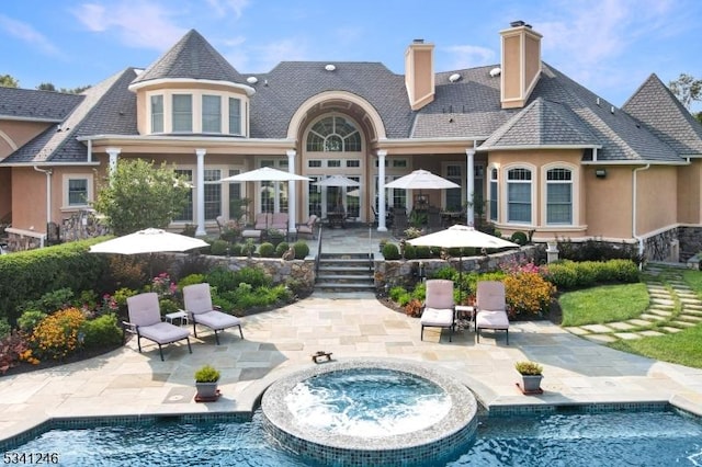 rear view of house featuring a chimney, a patio area, a pool with connected hot tub, and stucco siding