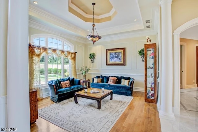 interior space featuring arched walkways, a raised ceiling, a decorative wall, and ornate columns