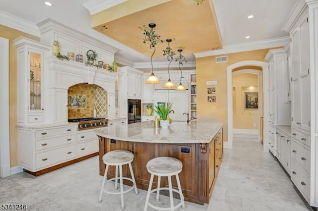 kitchen featuring visible vents, arched walkways, glass insert cabinets, ornamental molding, and a kitchen breakfast bar