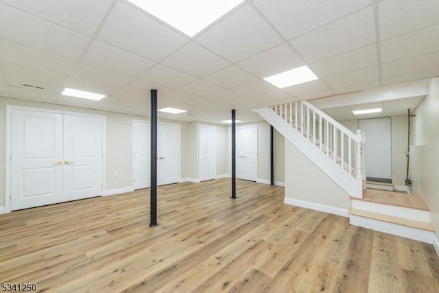 finished basement with stairs, wood finished floors, baseboards, and a paneled ceiling