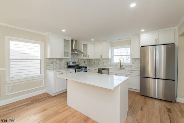 kitchen featuring wall chimney range hood, light wood-style flooring, stainless steel appliances, white cabinetry, and a sink