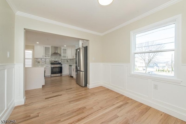 interior space with a decorative wall, a wainscoted wall, light wood finished floors, and ornamental molding