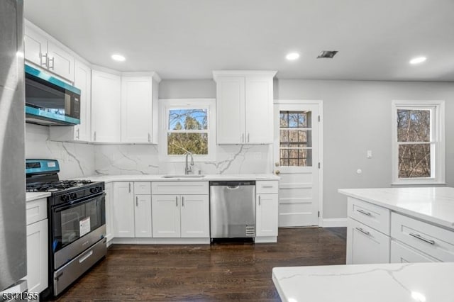 kitchen featuring light stone counters, stainless steel appliances, dark wood-style flooring, a sink, and white cabinets