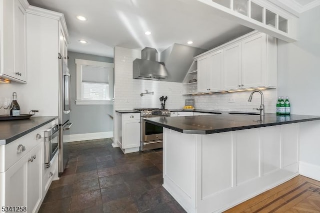 kitchen featuring stainless steel appliances, dark countertops, a sink, and wall chimney exhaust hood