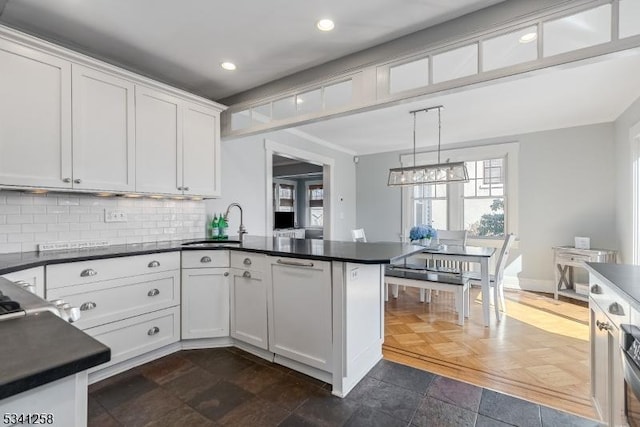 kitchen with decorative backsplash, dark countertops, a peninsula, white cabinetry, and a sink