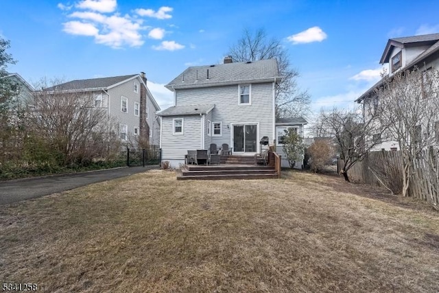 rear view of house featuring fence, roof with shingles, a lawn, a wooden deck, and a chimney