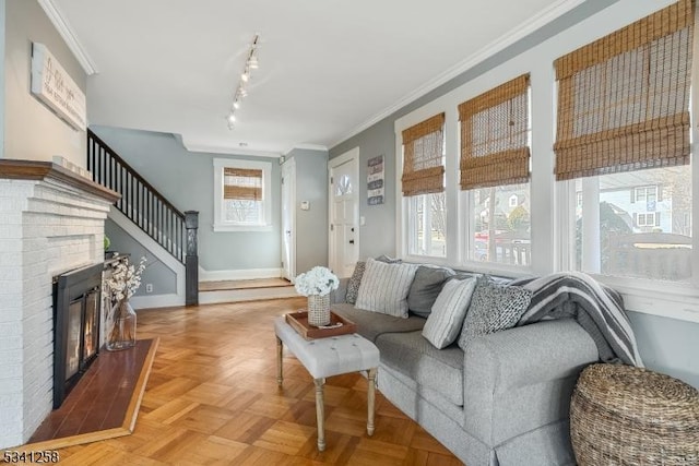 living area with crown molding, a fireplace, baseboards, stairs, and track lighting