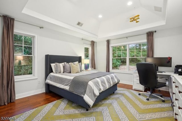 bedroom with a tray ceiling, visible vents, baseboards, and wood finished floors