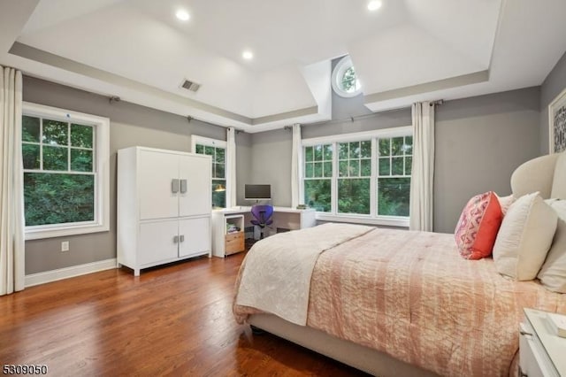 bedroom with a tray ceiling, wood finished floors, visible vents, and multiple windows