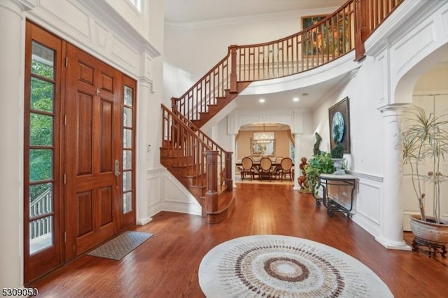 foyer with arched walkways, ornamental molding, wood finished floors, ornate columns, and a decorative wall