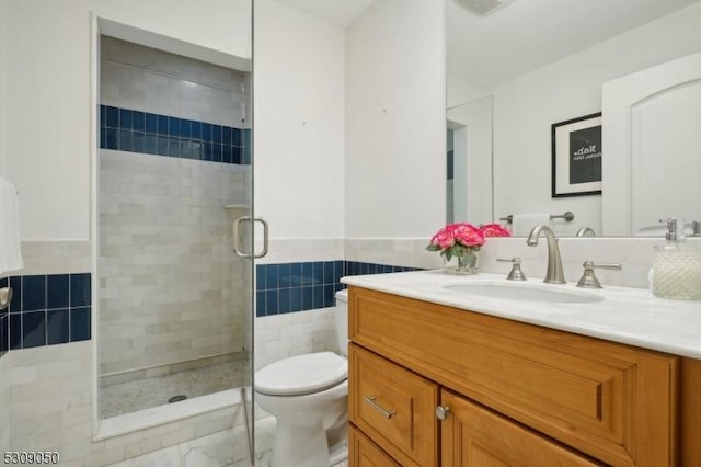 full bathroom featuring a stall shower, wainscoting, toilet, vanity, and tile walls