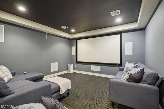 cinema room with a tray ceiling, visible vents, and carpet flooring