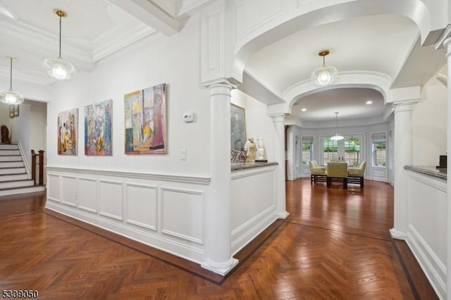 hall with arched walkways, ornamental molding, decorative columns, and a decorative wall