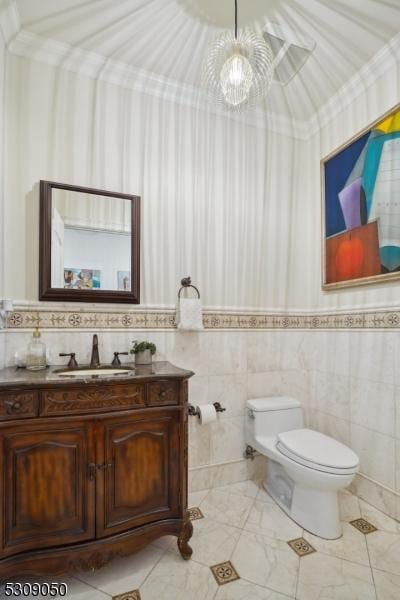 half bathroom with tile walls, vanity, toilet, and crown molding