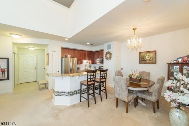 kitchen featuring light stone counters, light colored carpet, a kitchen breakfast bar, hanging light fixtures, and appliances with stainless steel finishes