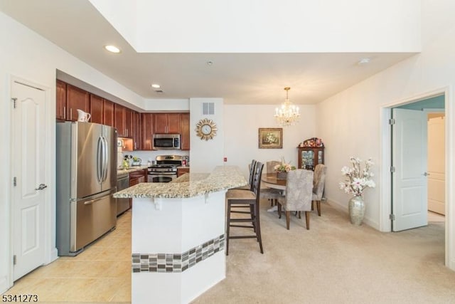 kitchen featuring light stone counters, a breakfast bar area, visible vents, hanging light fixtures, and appliances with stainless steel finishes