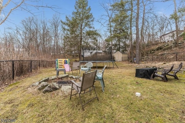 view of yard featuring a fire pit, a shed, a trampoline, and a fenced backyard