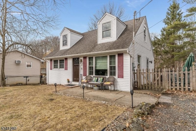 cape cod-style house featuring a front lawn, roof with shingles, a patio area, and fence