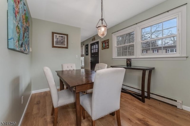 dining space featuring a baseboard radiator, wood finished floors, and baseboards