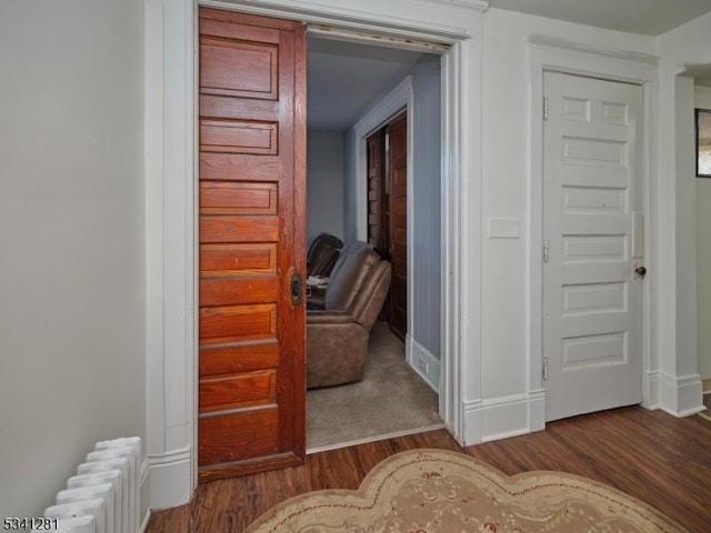 hallway with radiator heating unit, baseboards, and wood finished floors