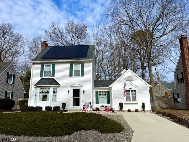 view of front of property featuring roof with shingles, a chimney, and solar panels