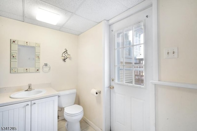 bathroom with vanity, baseboards, a drop ceiling, tile patterned floors, and toilet