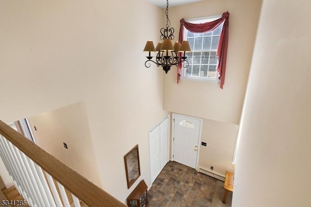 foyer entrance with a high ceiling, a notable chandelier, baseboard heating, and stone finish floor