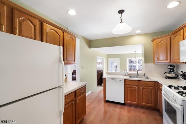 kitchen featuring hanging light fixtures, brown cabinets, white appliances, and a sink