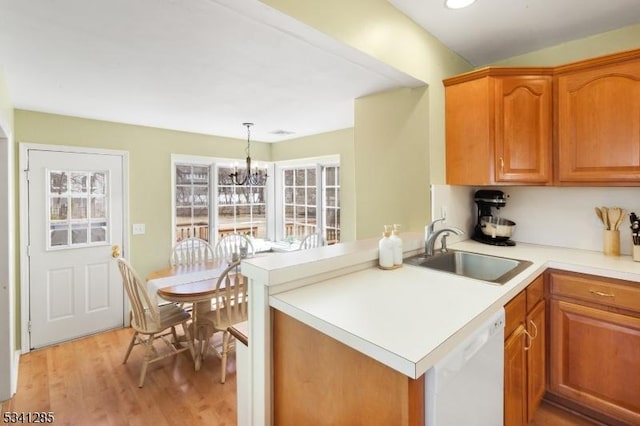 kitchen with a peninsula, an inviting chandelier, light wood-style floors, white dishwasher, and a sink