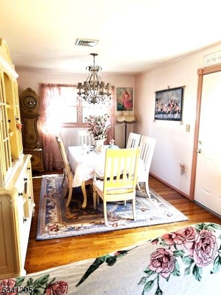 dining room with wood finished floors, visible vents, and an inviting chandelier