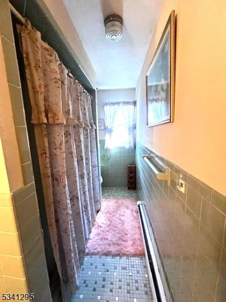 hall with wainscoting, tile walls, and tile patterned floors