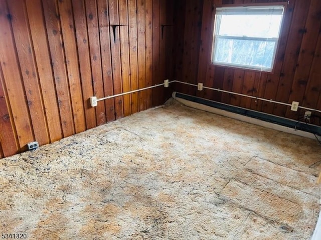 spare room featuring carpet floors, wood walls, and a baseboard radiator