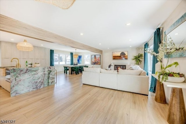 living area with light wood finished floors, recessed lighting, beam ceiling, and a glass covered fireplace