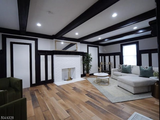 living area with beam ceiling, a fireplace, and wood finished floors