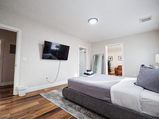 bedroom featuring baseboards, visible vents, wood finished floors, and ensuite bathroom