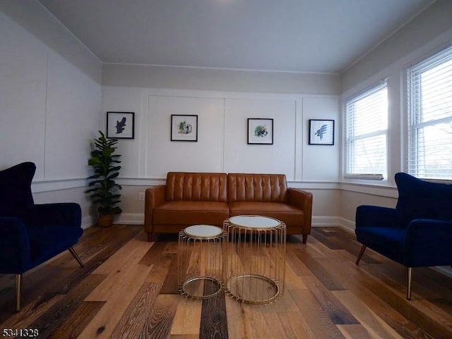 living area featuring baseboards, a decorative wall, and hardwood / wood-style floors