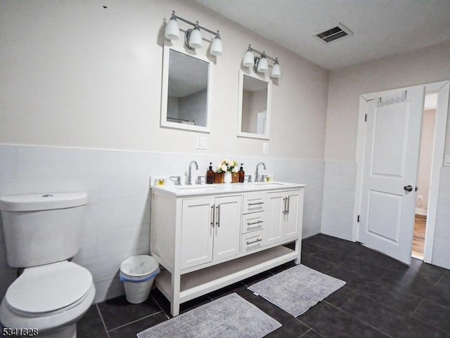 full bathroom with toilet, visible vents, a sink, and wainscoting