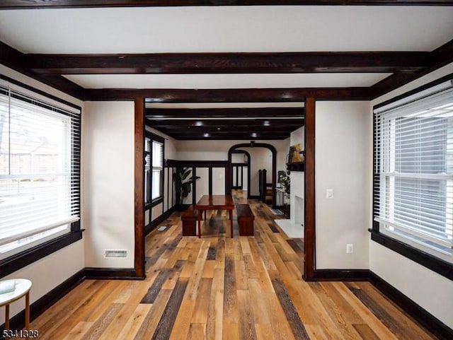 hallway with arched walkways, visible vents, light wood-type flooring, beamed ceiling, and baseboards