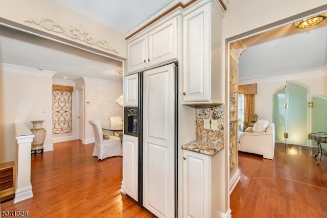 kitchen featuring light wood finished floors, paneled fridge, arched walkways, and ornamental molding