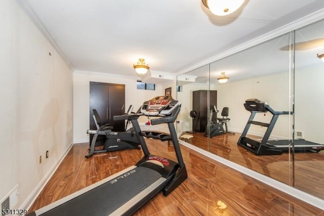 exercise area featuring baseboards, visible vents, ornamental molding, and wood finished floors